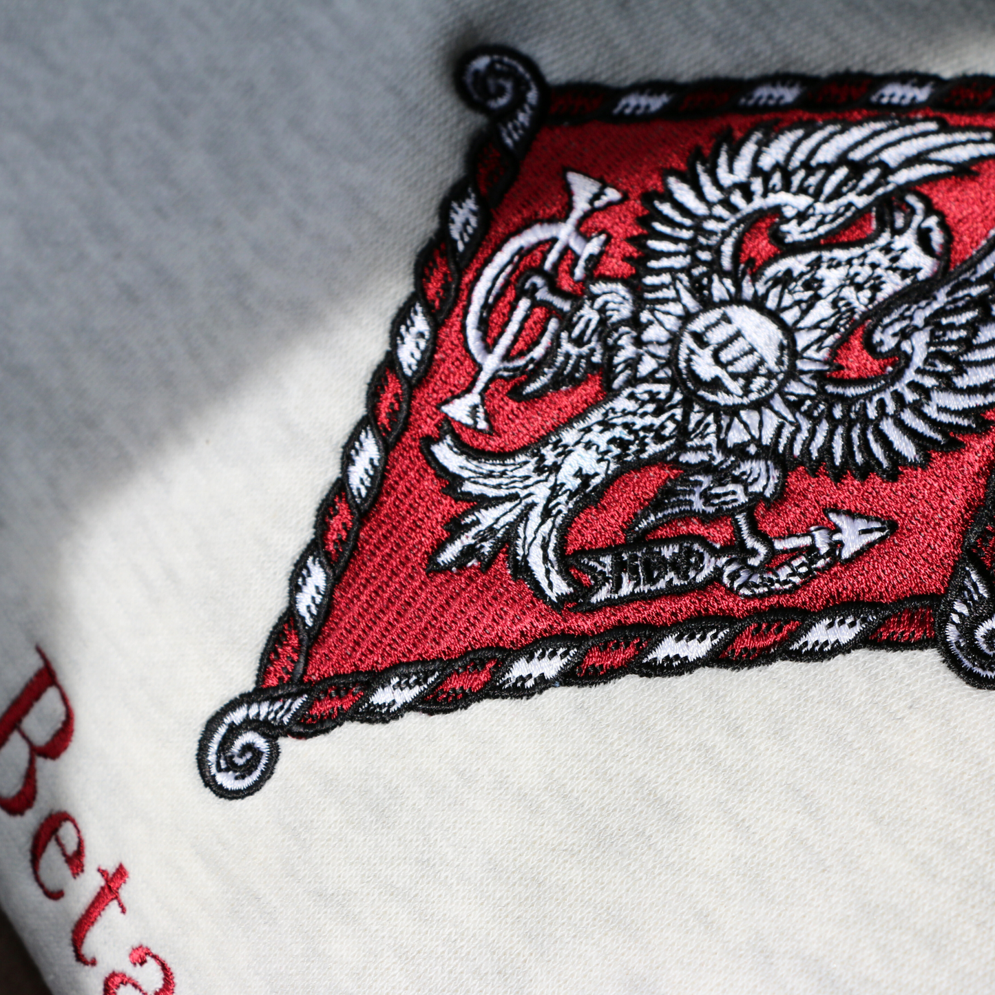 Detailed view of Pi Beta Phi's crest embroidered on a light grey sweatshirt. Featuring an eagle, the seal of Monmouth College, the blazing sun with the latin word lux within, and the Brownlee family crest. Below, the sorority name is embroidered.