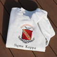 Load image into Gallery viewer, Sigma Kappa's crest embroidered on a light grey sweatshirt. Featuring a maroon shield with a diagonal gold bar on which are five stars. The lower half has a coiled serpent, and the upper has a maroon and gold wreath. Below, the sorority's name is embroidered in black.