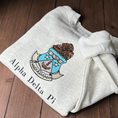 Load image into Gallery viewer, Gray crewneck sweatshirt featuring the Alpha Delta Pi sorority crest embroidered in the center. The crest includes a brown lion atop a blue shield with white stars. Below, the sorority name is embroidered in black.
