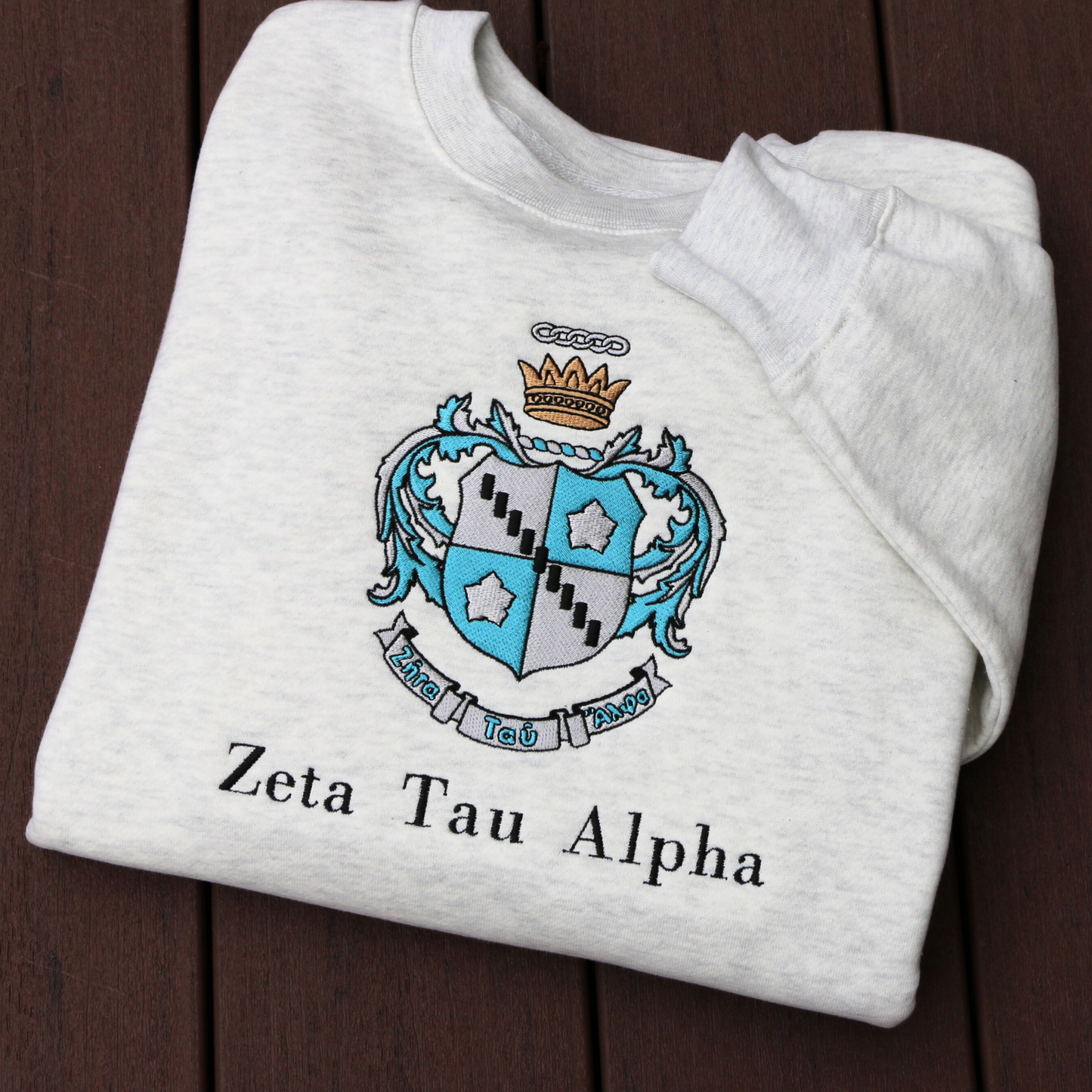 Zeta Tau Alpha's crest embroidered on a light grey sweatshirt. Featuring a silver and blue shield with a five pointed crown. The sorority name 'Zeta Tau Alpha' is embroidered in black beneath.