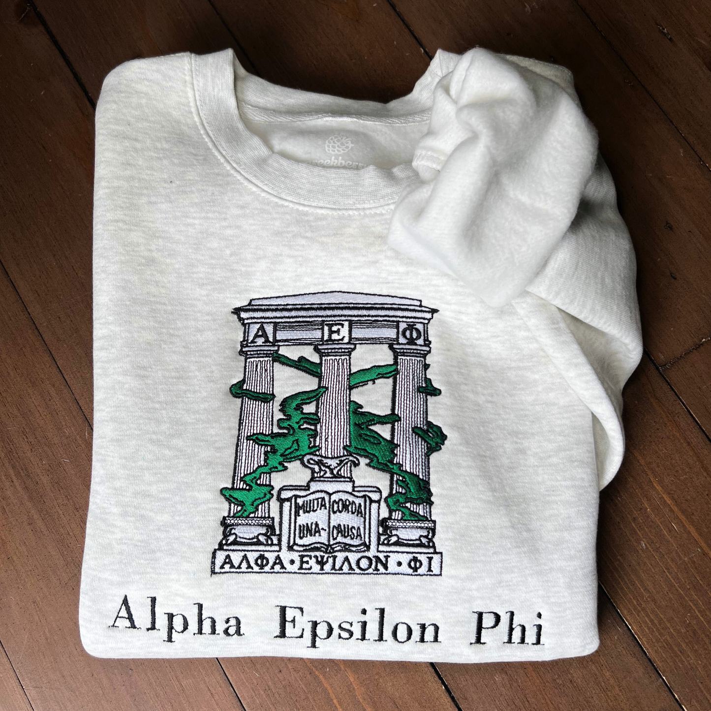 Folded light gray sweatshirt with an embroidered design of Alpha Epsilon Phi's emblem featuring white columns and green foliage. The columns support a structure with the Greek letters 'ΑΕΦ'. Below, the motto 'Multa Corda, Una Causa' is prominently displayed.