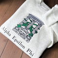 Load image into Gallery viewer, Folded light gray sweatshirt with an embroidered design of Alpha Epsilon Phi's emblem featuring white columns and green foliage. The columns support a structure with the Greek letters 'ΑΕΦ'. Below, the motto 'Multa Corda, Una Causa' is prominently displayed.