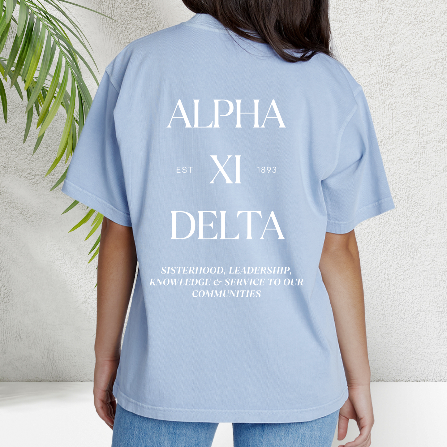 A woman wearing a light blue t-shirt with the Greek letters of her sorority spelled out with the sorority values below in white on the back.
