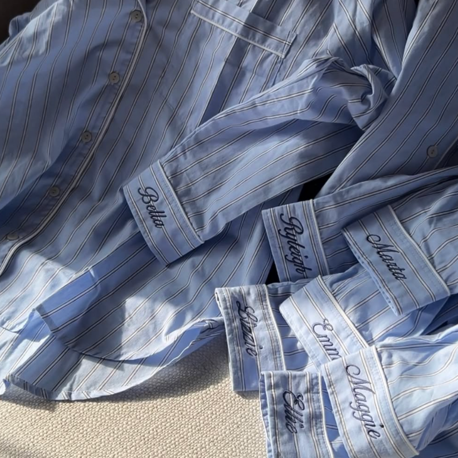 Blue striped shirts with names embroidered on the sleeves, laid out on a surface.